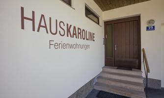 An entrance to "Haus Karoline" with a sign for vacation apartments. The steps lead to the wooden door of the building.