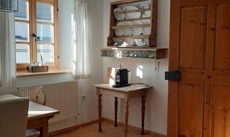 A bright, cozy room with wooden flooring. There is a table, chairs, and a display cabinet with dishes on the wall.