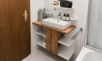A modern bathroom with a sink on a wooden shelf. The walls are brightly tiled, and there is a shower as well as a large mirror.