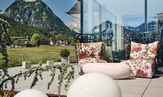 A modern terrace with cozy seating and a beautiful view of the mountains. The space is elegantly designed with floral patterns and round decorative objects.