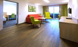 A modern hotel room with a red sofa and yellow chairs. Large windows offer a view and plenty of daylight.