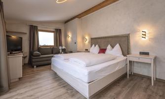 A cozy bedroom with a large bed and modern furniture. The room has windows with curtains and a flat-screen TV.