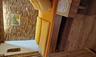 A cozy bedroom with a wooden bed and yellow bedding. The walls are adorned with stone cladding, and a picture hangs on the wall.