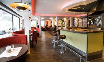 A modern restaurant with a stylish bar area and cozy seating. The bright decor is complemented by soft lighting and an open environment.