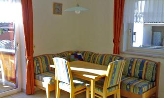 A cozy dining area with a padded seating area and a wooden table. Large windows provide plenty of daylight.