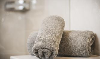 Two gray towels are stacked on top of each other on a white bath mat. The background is light and plain.