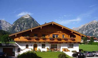 A traditional alpine house with a wooden facade and flower boxes. In the background, tall mountains and a clear sky can be seen.
