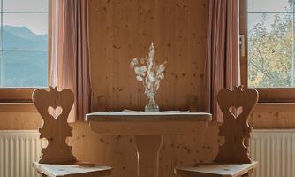A cozy room with wooden walls and large windows. At the table, there are two chairs with heart designs and a vase on the table.
