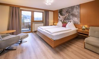 A modern hotel room with a large bed and comfortable furniture. The room has large windows that let in plenty of daylight.
