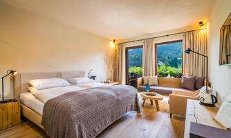 A modern bedroom with a large double bed and a cozy living area.  
Large windows offer a view of the mountains and plenty of natural light.