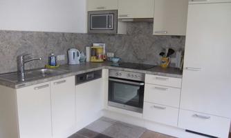 A modern kitchen with light cabinets and a gray countertop. It is equipped with a stove, a microwave, and various kitchen utensils.