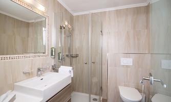 A modern bathroom with a shower and a sink. The walls are light and finished with beige wood veneer.