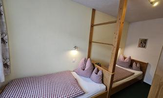 A cozy bedroom with two single beds and checked pillows. The walls are light, and there is a warm, inviting atmosphere.