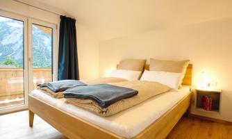 A modern bedroom with a large bed and comfortable pillows. The windows offer a view of the mountains and add a bright, inviting ambiance.