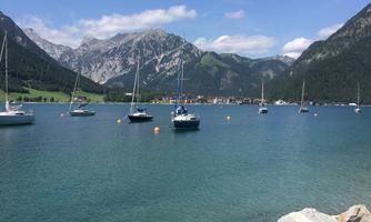 A quiet bay with several sailboats and clear blue water. In the background, impressive mountains rise under a bright blue sky.