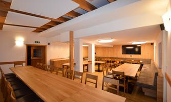 A modern space with long wooden tables and chairs. The walls are in warm tones, and there is pleasant lighting.