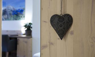 A decorative black heart hangs from a wooden ceiling. In the background, there is a plant pot and a picture of landscapes.