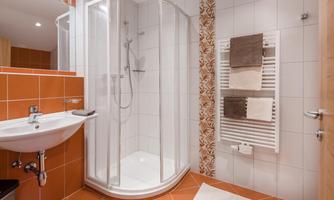A modern bathroom with a glass shower and orange tiles. Towels and a sink are also available.