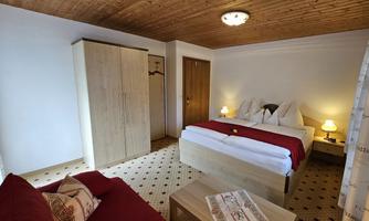 A cozy bedroom with a double bed and a red sofa. The room has wooden ceilings and a warm, inviting atmosphere.