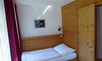 A simple bedroom with a single bed and wood paneling. A picture hangs on the wall, and the door is open.