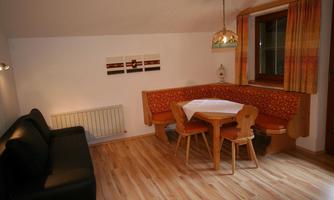 A cozy dining area with a wooden bench and table. The walls are painted in neutral colors, and there is a black couch for added comfort.