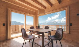 A cozy dining area with a wooden table and chairs. Large windows provide a beautiful view of the mountains and the blue sky.
