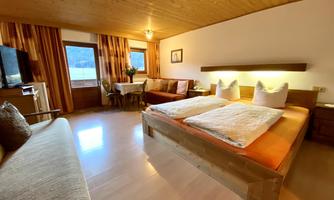 A cozy hotel room with two beds and a beautiful wooden ceiling. In front of the window, there is a view of the landscape.