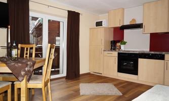 A modern kitchen with a dining area and wooden floor. The furniture is bright and inviting, with windows that let in plenty of light.