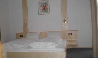 A simple bedroom with a double bed and two blankets. A small picture with floral motifs hangs on the wall.