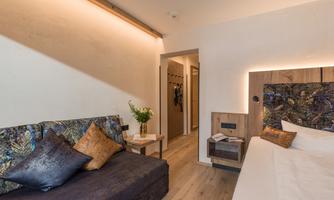 A stylish hotel room with a sofa and a cozy bed. The warm colors and subtle lighting create an inviting atmosphere.
