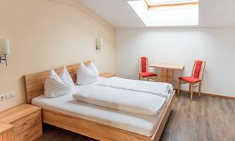 A modern room with a double bed and two red chairs. The room has a bright wooden floor and a skylight for natural light.