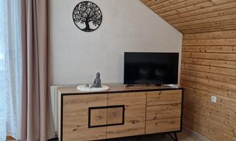 A modern living space with a wooden dresser and a television. Decorative wall art in the form of a tree hangs on the wall.