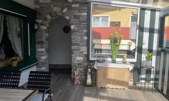 A bright conservatory with a stone arch and a wooden cabinet. Fresh flowers are on a table, and the decor is modern and inviting.