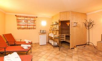 A relaxing wellness room with two loungers and a sauna. The walls are designed in warm colors, and there is a small refrigerator corner.
