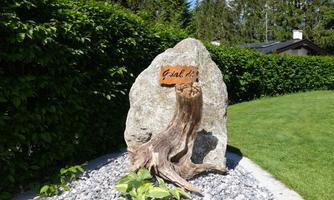 A large stone with a wooden plaque that says "Go here." Surrounded by a green hedge and a lawn area.