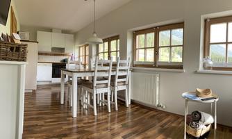 A bright dining area with a large table and light wood chairs.  
Large windows provide plenty of daylight and a cozy atmosphere.