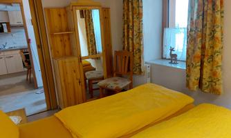 A cozy bedroom with two yellow beds. In the background, a mirror, a chair, and a window with curtains can be seen.