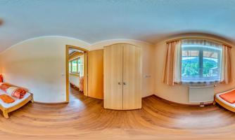 A bright room with two single beds, wooden flooring, and large windows. The walls are painted in warm colors, and there is a wardrobe.