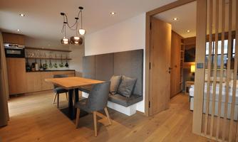 A modern apartment with a wooden dining area and a cozy seating corner. The room is well-lit and has a warm, inviting style.