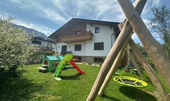 A beautiful garden with a playground. In the background, there is a modern house under a blue sky.