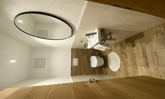 A modern bathroom with a white toilet and an elegant sink. The walls are bright and the floor is made of wood, with a round mirror above the sink.