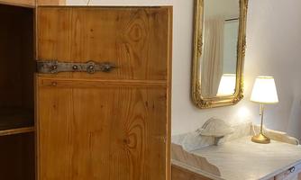 A rustic room with a wooden wardrobe and an elegant mirror. A lamp and decorative elements give the room coziness.