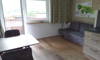 A bright living room with a cozy sofa and a dining area. Large windows offer a view of the outdoor area and let in plenty of light.