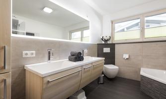 A modern bathroom with light wood and neutral colors. It features a sink, a toilet, and a large mirror.