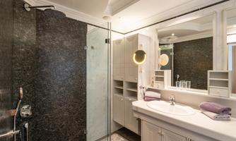 A modern bathroom with a glass shower and elegant fixtures. The space is bright and neutrally designed, with white furniture and dark stone accents.