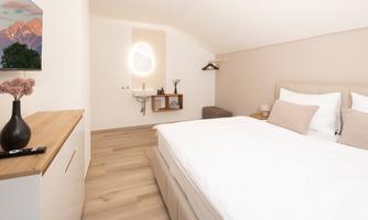 A modern bedroom with a large bed and soft colors. On the left side, there is a television and a stylish wall picture.