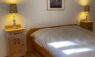 A cozy bedroom with a wooden bed and warm light from bedside lamps. A picture hangs on the wall, and the floor is made of wood.