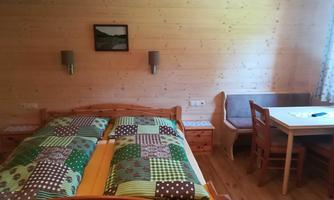 A cozy bedroom with a wooden bed and colorful bedcovers. Next to it is a table with chairs and a wooden bench.