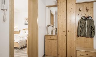 A bright hallway with a wooden wardrobe and a jacket. A bedroom is visible in the background.