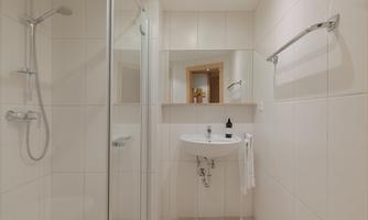 A modern bathroom with a shower cabin and a small sink. The walls are tiled in bright white.